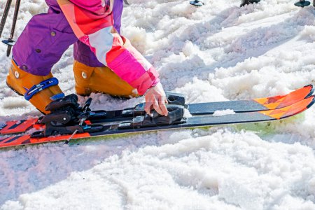 esquiador se pone sus botas de esquí en una ladera nevada en un día soleado. Vacaciones familiares activas