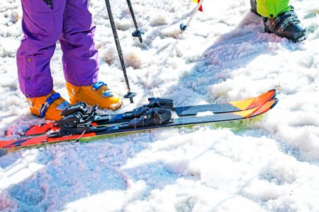 skieur met ses chaussures de ski sur une pente enneigée par une journée ensoleillée. Vacances actives en famille