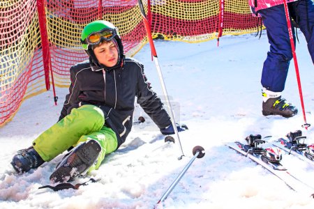 Téléchargez les photos : Skieur met ses chaussures de ski sur une pente enneigée par une journée ensoleillée. Vacances actives en famille - en image libre de droit