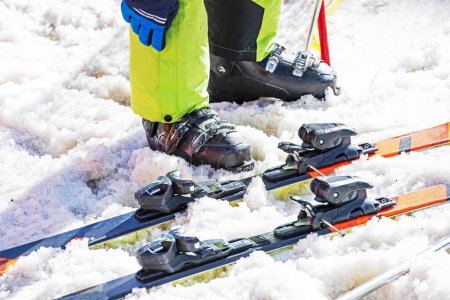 Skifahrer schnürt an einem sonnigen Tag seine Skischuhe an einem verschneiten Hang. Aktiver Familienurlaub