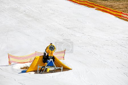 Foto de Generador de nieve amarillo en una pendiente de nieve en un complejo en un día soleado. Recreación activa - Imagen libre de derechos