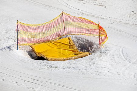 hoyo de tierra cubierto con una alfombra amarilla vallada con una red en una pendiente nevada, Seguridad y recreación activa con la familia