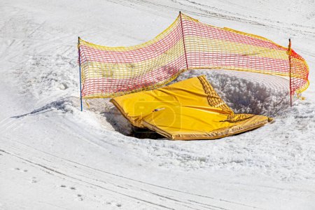 Erdgrube mit einer gelben Matte umzäunt mit einem Netz auf einem schneebedeckten Hang, Sicherheit und aktive Erholung mit der Familie