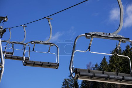 empty ski lift against the background of blue sky and fir trees. Active recreation