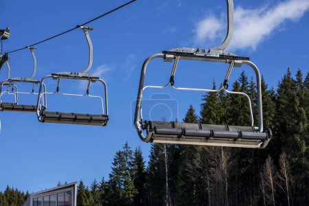 Leerer Skilift vor blauem Himmel und Tannenbäumen. Aktive Erholung
