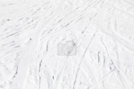 abstrakter Hintergrund aus weißem Schnee mit Spuren von Skifahrern an einem sonnigen Tag