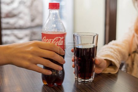 Photo for Girls holding a glass of Coca-Cola in a cafe in Ivano Frankovs, in Ukraine March 31, 2024 - Royalty Free Image