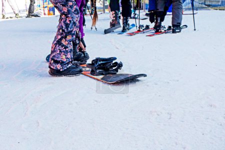 skiers and snowboarders re-strap their boots for a moderately difficult ski slope. Leisure