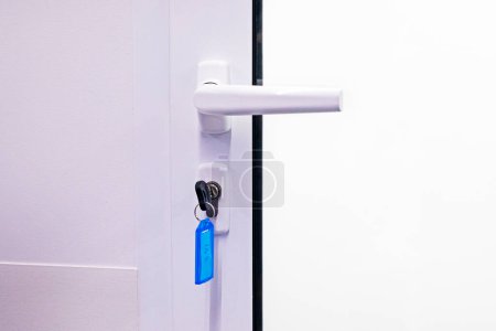 Metallgriff an weißer geschlossener Tür mit installiertem Schlüssel. Moderner Innenraum