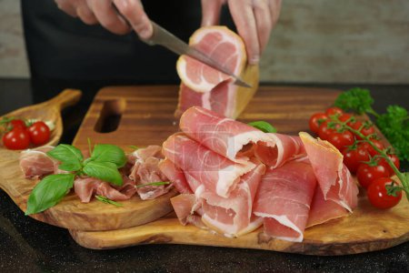 Téléchargez les photos : Cutting slices of dry ham on a wooden board, meat slices on wooden board concept - en image libre de droit