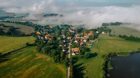 Téléchargez les photos : Aerial view of small village in fog.Top view of traditional housing estate in Czech. Looking straight down with a satellite image style.Houses from above, real estate concept.Country road urban scene. - en image libre de droit