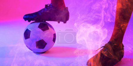 Photo for Low section of male player wearing black sport shoes with leg on ball against colorful smoke. Copy space, composite, sport, soccer, competition, neon and abstract concept. - Royalty Free Image