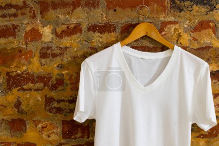 Foto de Camiseta colgando en percha y espacio de copia sobre fondo de ladrillo. Ropa, moda y concepto de retail. - Imagen libre de derechos