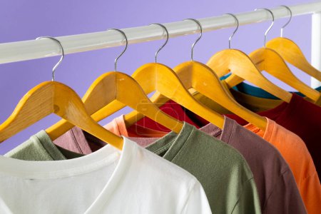Foto de Camisetas de colores que se muestran en el carril de la ropa y espacio de copia sobre fondo púrpura. Ropa, moda y concepto de retail. - Imagen libre de derechos
