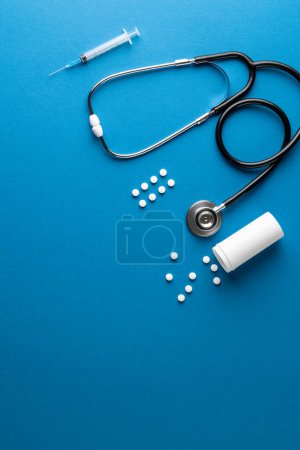 Photo for Vertical composition of stethoscope with pills and syringe on blue background with copy space. Medical services, healthcare and health awareness concept. - Royalty Free Image