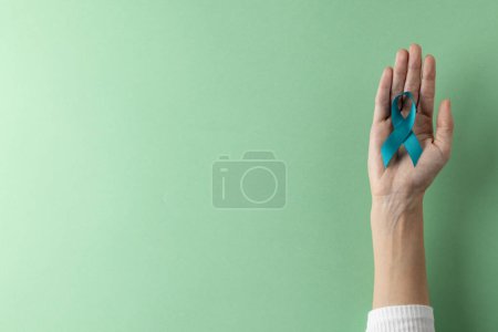 Téléchargez les photos : Composition de la main tenant le ruban bleu de sensibilisation au cancer de l'ovaire sur fond vert avec espace de copie. Services médicaux, santé et sensibilisation à la santé concept. - en image libre de droit
