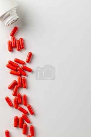 Foto de Composición vertical de la caja de pastillas blanca derramando píldoras rojas sobre fondo blanco con espacio de copia. Medicina, servicios médicos, salud y concepto de concienciación en salud. - Imagen libre de derechos