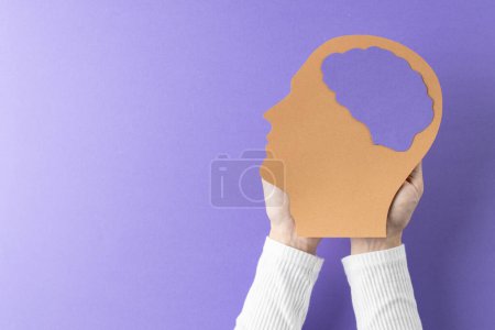 Photo for Composition of hands holding head silhouette with purple brain on purple background, with copy space. Medical services, healthcare and mental health awareness concept. - Royalty Free Image