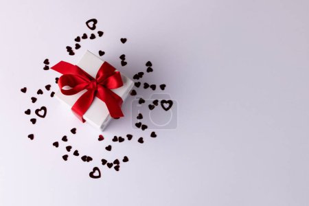 Téléchargez les photos : Coffret cadeau blanc avec ruban rouge sur confettis coeur, sur fond blanc avec espace de copie. Saint Valentin, amour, romance et concept de célébration. - en image libre de droit