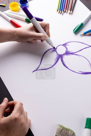 Téléchargez les photos : Image verticale des mains dessinant fleur violette sur papier et matériaux d'art sur le dessus de table, espace de copie. Art, créativité, mois artisanal et concept de passe-temps. - en image libre de droit