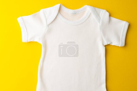 Foto de Primer plano de la camiseta blanca bebé con espacio de copia sobre fondo amarillo. Ropa y accesorios, concepto de cuidado de niños recién nacidos e infantes. - Imagen libre de derechos