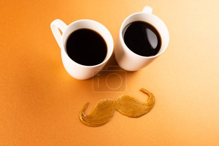 Téléchargez les photos : Composition de moustache fausse et tasses de café sur fond orange avec espace de copie. Fausse moustache jour, fête, célébration et concept de costume. - en image libre de droit