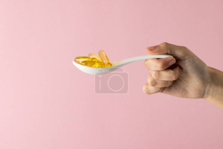 Photo for Composition of hand holding spoon with oil capsules on pink background with copy space. Medicine, medical services, healthcare and health awareness concept. - Royalty Free Image