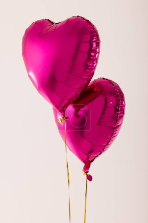 Photo for Vertical of two shiny pink heart shaped balloons floating on white background with copy space. Valentine's day, love, romance and celebration concept. - Royalty Free Image