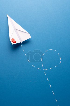 Photo for Vertical of paper plane with red heart and white trail, on blue background with copy space. Valentine's day, love, romance, communication and celebration concept. - Royalty Free Image