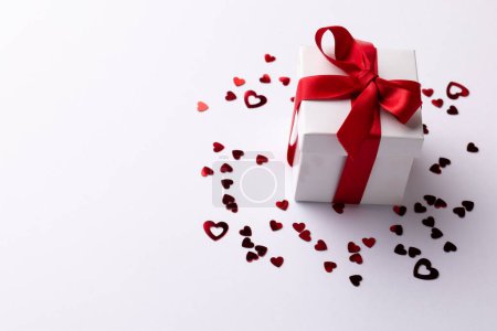 Téléchargez les photos : Coffret cadeau blanc avec ruban rouge sur confettis coeur, sur fond blanc avec espace de copie. Saint Valentin, amour, romance et concept de célébration. - en image libre de droit
