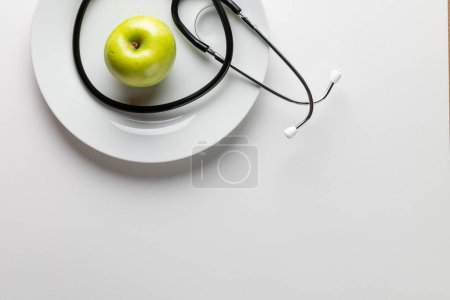 Photo for Composition of stethoscope and apple on plate, on white background with copy space. Medical services, healthcare and health awareness concept. - Royalty Free Image