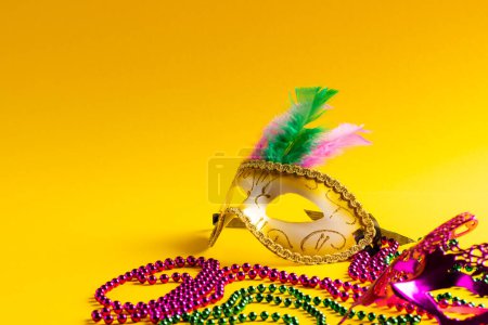 Foto de Composición de coloridas cuentas de mardi gras y máscaras de carnaval sobre fondo amarillo con espacio para copiar. Fiesta, celebración y concepto de carnaval. - Imagen libre de derechos