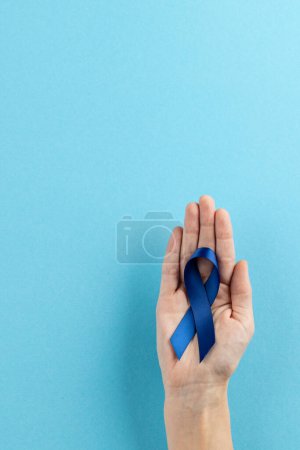 Foto de Vertical de la mano que sostiene la cinta azul de la conciencia del cáncer del colon en el fondo azul con el espacio de la copia. Servicios médicos, asistencia sanitaria y concepto de concienciación sanitaria. - Imagen libre de derechos