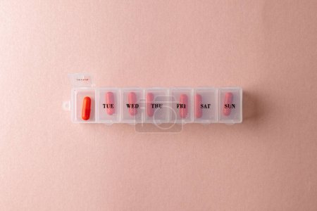 Téléchargez les photos : Composition des pilules rouges dans une boîte à pilules hebdomadaire sur fond rose avec espace de copie. Médecine, services médicaux, santé et sensibilisation à la santé. - en image libre de droit