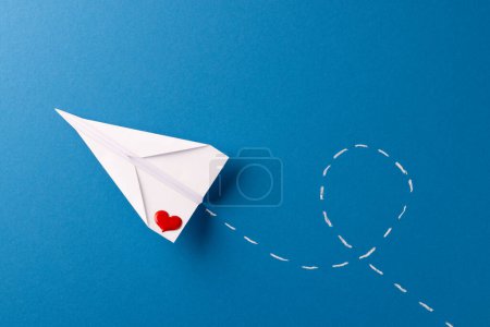 Téléchargez les photos : Avion en papier avec coeur rouge et traînée blanche, sur fond bleu avec espace de copie. Saint Valentin, amour, romance, concept de communication et de célébration. - en image libre de droit