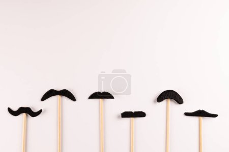 Téléchargez les photos : Composition de fausses moustaches sur bâtons sur fond blanc avec espace de copie. Fausse moustache jour, fête, célébration et concept de costume. - en image libre de droit