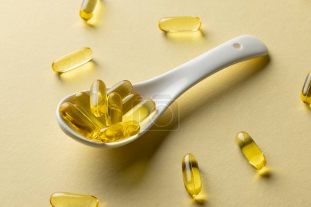 Photo for Composition of oil capsules and white spoon on yellow background. Medicine, medical services, healthcare and health awareness concept. - Royalty Free Image