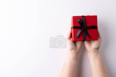 Téléchargez les photos : Mains tenant boîte cadeau rouge attaché avec ruban noir, sur fond blanc avec espace de copie. Saint Valentin, anniversaire, amour, romance et concept de célébration. - en image libre de droit