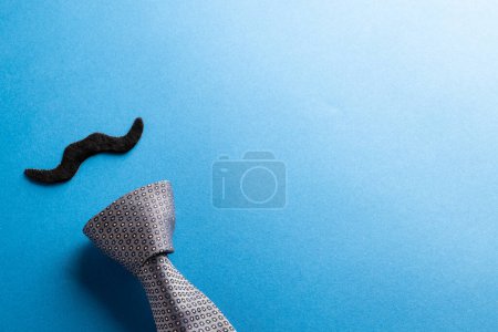 Téléchargez les photos : Composition de fausse moustache et cravate sur fond bleu avec espace de copie. Fausse moustache jour, fête, célébration et concept de costume. - en image libre de droit