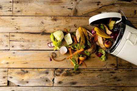 Photo for Organic fruit and vegetable food waste spilling from open kitchen composting bin. On wooden boards with copy space. Ecology, recycling, care and nature concept. - Royalty Free Image