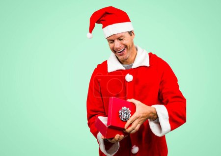 Photo for Caucasian man wearing santa costume opening christmas gift against copy space on green background. christmas and festivity concept - Royalty Free Image