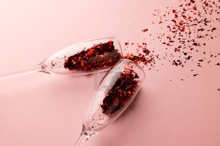 Photo for Two champagne glasses spilling red glitter confetti on pale pink background with copy space. Valentine's day, love, romance and celebration concept. - Royalty Free Image