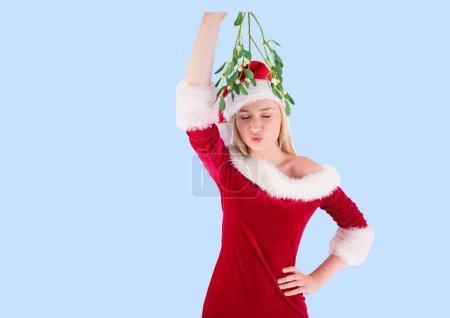 Photo for Caucasian woman wearing santa costume holding a mistletoe against copy space on blue background. christmas festivity concept - Royalty Free Image