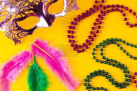 Téléchargez les photos : Composition de perles de mardi gras, plumes et masque de carnaval sur fond jaune avec espace de copie. Fête, célébration et concept de carnaval. - en image libre de droit