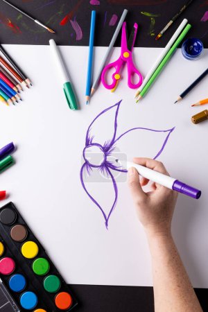 Foto de Imagen vertical de dibujo a mano flor púrpura en papel y materiales de arte en la mesa, espacio de copia. Arte, creatividad, artesanía y concepto de pasatiempos. - Imagen libre de derechos