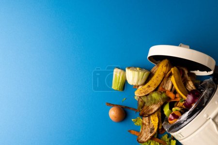 Téléchargez les photos : Déversement de déchets alimentaires de fruits et légumes biologiques provenant de la poubelle de compostage de cuisine ouverte. Sur fond bleu avec espace de copie. Concept écologie, recyclage, soins et nature. - en image libre de droit