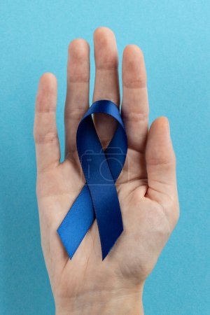 Photo for Vertical of hand holding blue colon cancer awareness ribbon on blue background with copy space. Medical services, healthcare and health awareness concept. - Royalty Free Image