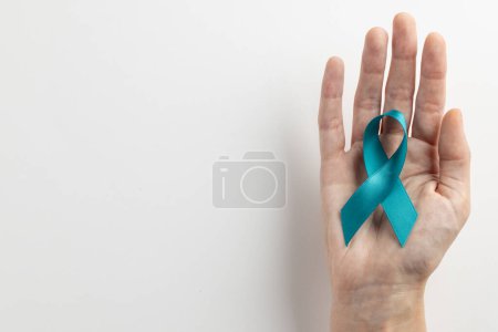 Foto de Composición de la mano que sostiene la cinta azul de la conciencia del cáncer de ovario en el fondo blanco con el espacio de copia. Servicios médicos, asistencia sanitaria y concepto de concienciación sanitaria. - Imagen libre de derechos