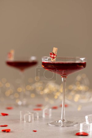 Photo for Vertical of two red cocktails with heart shape clips and string lights, selective focus, copy space. Valentine's day, love, romance and celebration concept. - Royalty Free Image