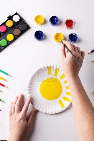 Photo for Vertical of hands painting with yellow on paper plate and art materials on table top, copy space. Art, creativity, craft month and hobbies concept. - Royalty Free Image